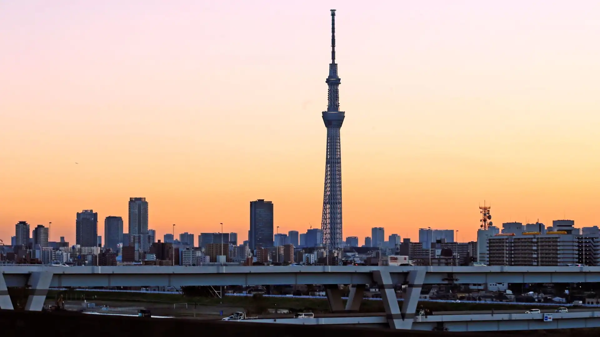 Tokyo Skytree se za soumraku tyčí nad řekou Sumidou, její příhradová věž osvětlená na pozadí tokijské panoramy